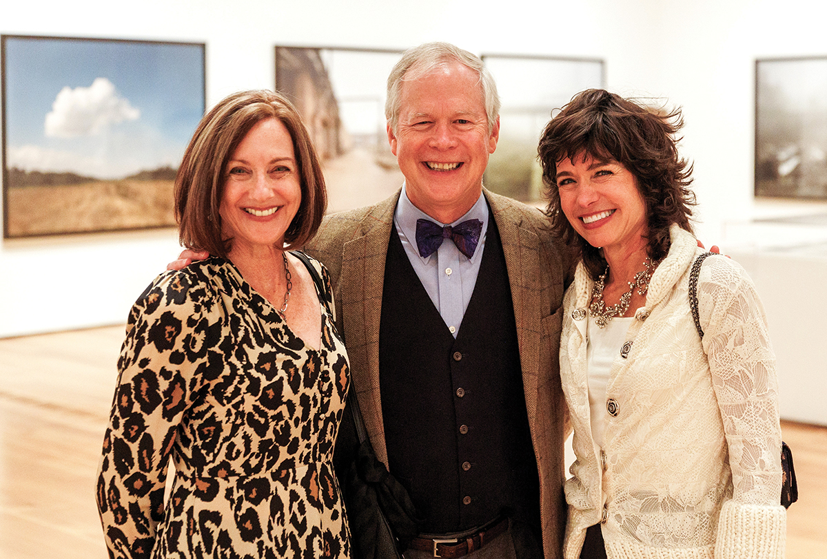 Three people pose together in a gallery of large photographs.