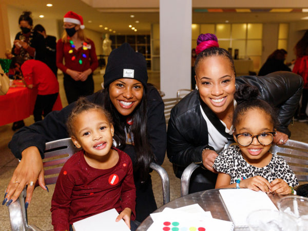 Two women lean over two small children seated at a cafe table and smile at the camera.