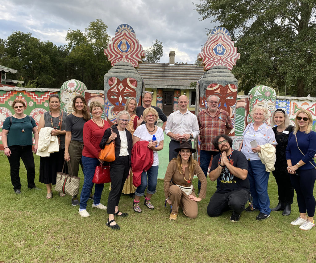 A group of people pose for the camera outdoors in front of a large concrete gate and fence painted with elaborate designs.