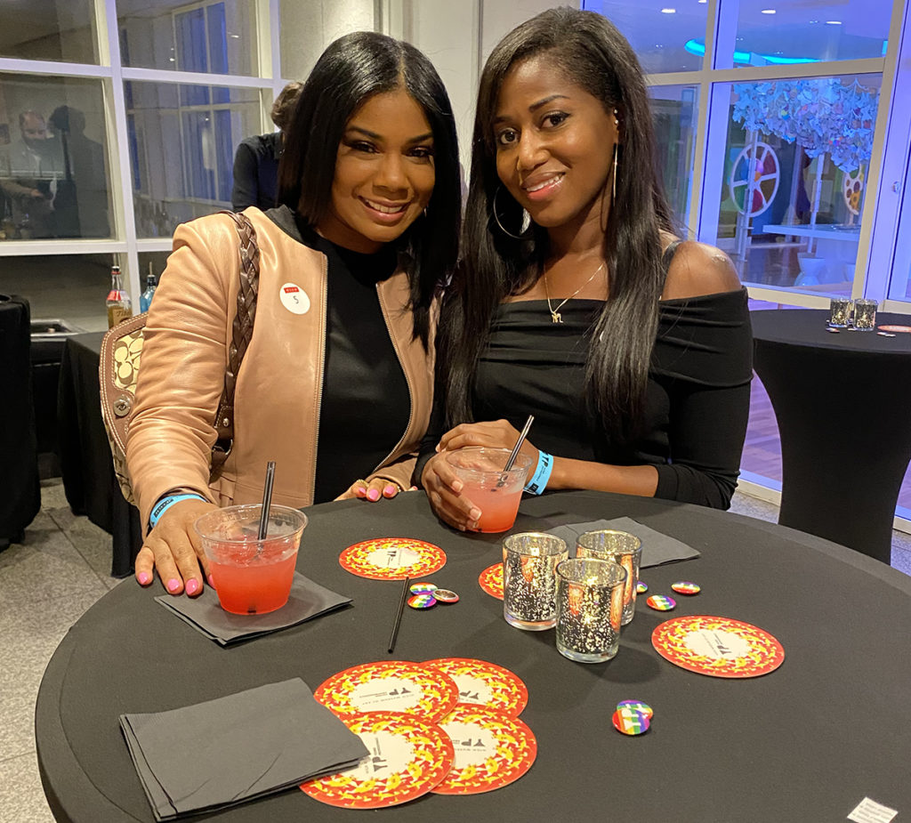 Two women smile at the camera with their drinks resting on a table in front of them.