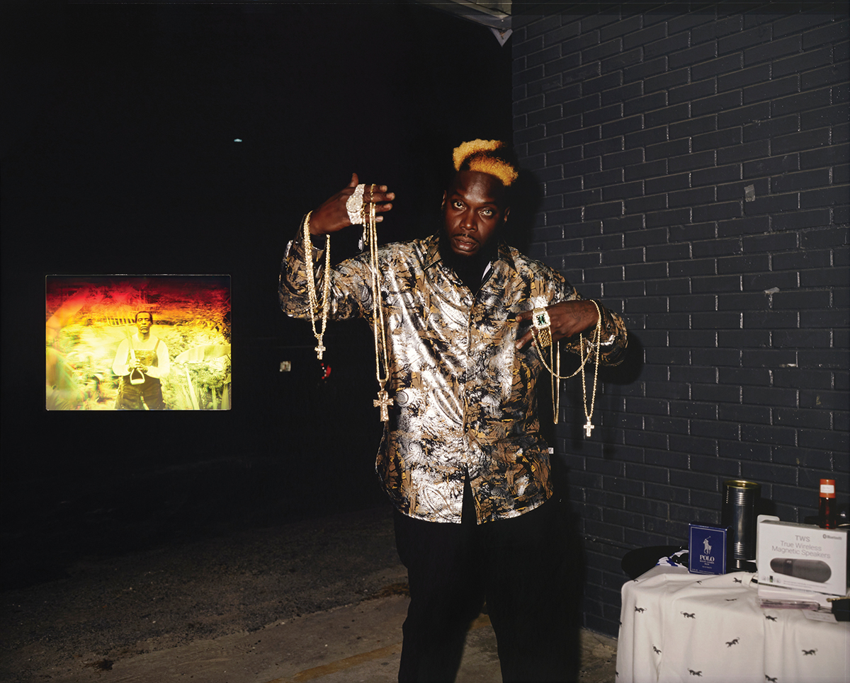 A photograph of a Black man holding up jewelry while a photograph behind him shows a Black man in a field holding up a garden tool.