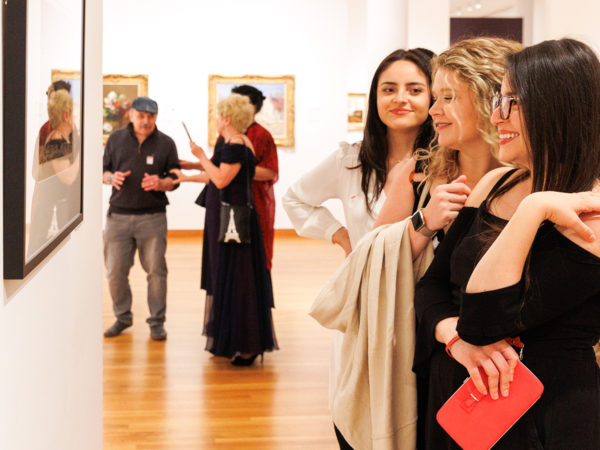 Three people stand together in front of a framed print in a gallery.