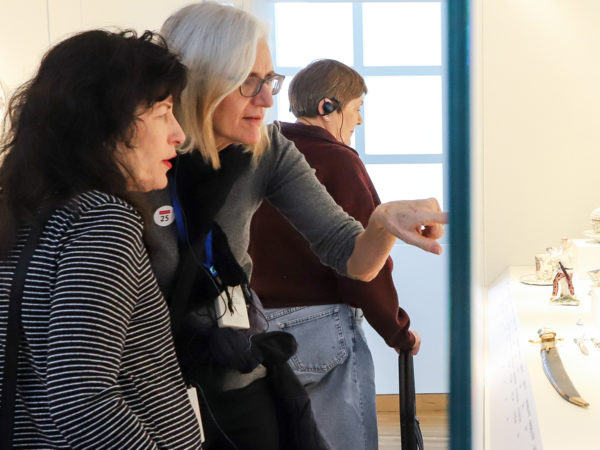 A museum visitor points out an object behind glass to another person as they view decorative objects in a gallery.